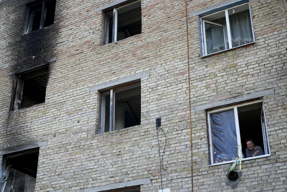 A woman looks outside her window at a building destroyed by attacks in Gorenka, on the outskirts of Kyiv, Ukraine, Wednesday, June 8, 2022. (AP Photo/Natacha Pisarenko)